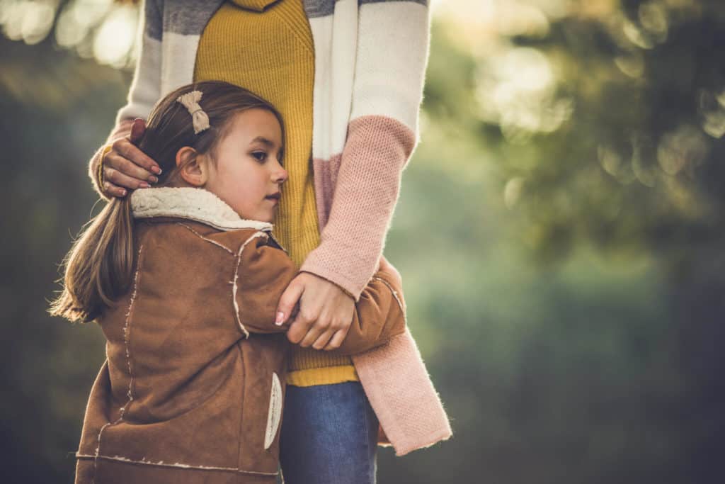 Little girl feeling protected in her mother's embrace outdoors.