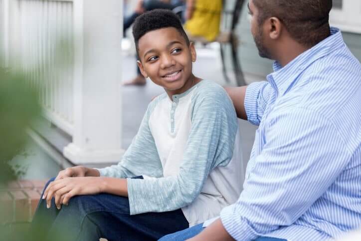 Confident mid adult African American father encourages his son while giving him advice about life. They are sitting on the front porch of their home.