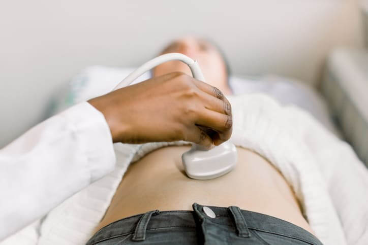 Cropped image of female African doctor hand moving ultrasound transducer on woman's stomach