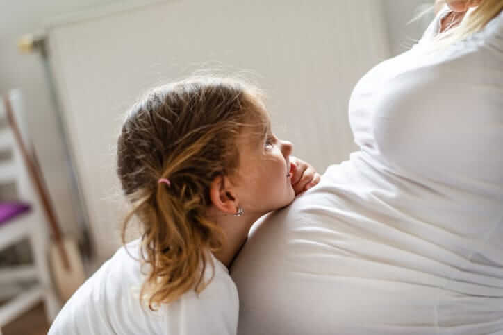 Close -up of a beautiful girl hugging mother’s pregnant belly with a smile.