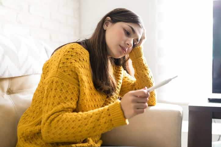 Stressed Latin woman looking at positive pregnancy test kit at home